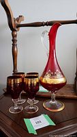 Photo showing the whole set with one tall red and clear glass decanter with gold detailing and four matching glasses.