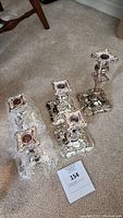 Three silver-toned ornate candle holders positioned on a carpet, all featuring decorative grapevine and floral embossed patterns at the base and stem with square-shaped top candle holders.