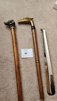 Photo showing three wooden walking sticks with animal head handles: dog, eagle brass, and carved dark animal head.