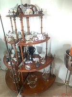 Photo of triangular wooden corner display cabinet with multiple shelves showing various decorative glass and ceramic figurines on shelves.