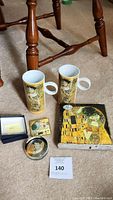 Overview photo showing all six items from the Gustav Klimt collection including two mugs, two square boxes, compact mirror, and boxed pin.
