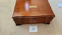 Closed wooden jewelry box with curved top and brass hardware on a carpeted floor.
