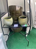 Shelf with multiple green ceramic planter pots of varying sizes and textures, stacked and arranged for display