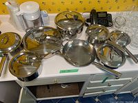 Top view of full cookware set arranged on a counter, showing multiple stainless steel pots and pans with their lids.