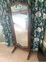 Full front view of the standing mirror showing the carved wooden frame and clear mirror surface.