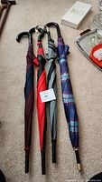 Four umbrellas displayed closed on carpet showing different handle styles and colors