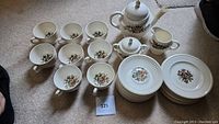 Complete tea set contents including cups, plates, teapot, creamer, and sugar bowl arranged on carpet.