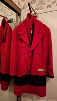 Front view of the women's XL red wool jacket with black trim hanging on hook showing button closure and chest flap pockets.