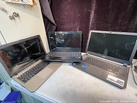 Three laptops displayed side by side on a surface: a silver HP laptop, a black Lenovo laptop, and a third silver laptop computer.