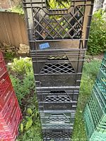 Stacked four black milk crates, each with lattice sides and the 'Nutr' brand name visible on the sides. Positioned outdoors on grass with some other colored crates nearby.