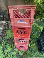 Four stacked red Sealtest plastic milk crates on grass outdoors, showing branding and condition.