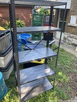 Photo of the metal shelving unit outside showing 5 black metal slotted shelves with vertical support posts.