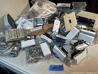 Photo showing a variety of electrical hardware including switches, outlets, electrical boxes, light sockets, and fittings on a white surface.