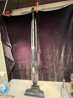 Full view of the Bissell Magic Vac upright vacuum cleaner against black backdrop, showing the entire length and design of the unit with handle and base.