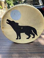 Front side of the native drum showing a painted wolf silhouette howling at a white moon on natural drum skin surface.