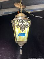 Overall view of the antique stained glass ceiling fixture hanging from chain with ceiling mount, showing metal shaped frame and yellow white stained glass panels with decorative metal overlay