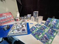 Wide shot showing large assortment of hockey cards, sticker collection box, protective sleeves, and boxed cards on a table.