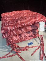 Stack of 4 red seat cushions with white stripes, showing some tie backs, some missing.