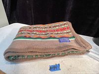Folded wool blanket showing colorful geometric stripes and a blue label patch.