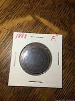 Photo of the obverse or reverse of the 1888 Canada one cent coin in a white cardboard coin protector labeled '1888 F' with visible wear on the coin surface.