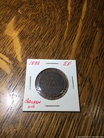 Reverse of 1892 Canadian one cent coin showing 'ONE CENT 1892' surrounded by wreath in cardboard holder.