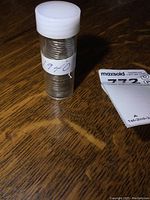 Plastic tube labeled '1940' filled with stacked Canadian nickels, placed on wooden surface.