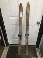 Full length view of both wooden skis standing upright showing overall condition and bindings