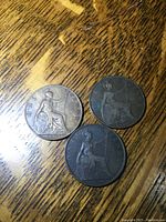Three large copper pennies, showing seated Britannia figure and dates: 1900, 1902, 1903, placed on wood surface.
