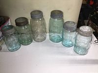 All six antique glass sealer jars in three sizes, five aqua colored and one clear, displayed with lids on.