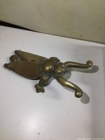Top angled view of vintage solid brass boot jack shaped like an insect with curved grips for pulling off boots, showing light tarnish.