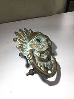 Close-up photo of the brass skull door knocker on a flat surface showing detailed skull face and ring, with tarnish on brass.