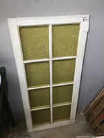 Full front view of old white wood window frame with eight yellow textured glass panes arranged in two columns and four rows.