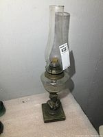 Full view of oil lamp showing chimney, burner, glass fuel reservoir, and figural base.