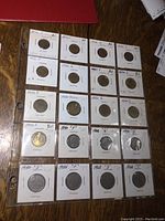 Page of foreign coins in white coin protectors with handwritten labels including years and grades. Coins range from 1950s to mid-1960s primarily.