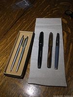 Image showing 3 vintage fountain pens laid flat next to a Parker boxed pen and pencil set with silver-tone writing instruments.