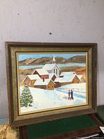Framed oil painting showing full scene of snowy village with church and figures in snow path
