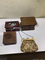 Three small wooden jewelry boxes and one gold sequin clutch purse on white surface