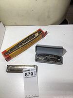 Tonette in box with two harmonicas, one in plastic case, one without case.