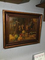 Framed oil painting of a rustic still life with vegetables, corn, bucket, straw hat, and hanging bird on wooden background.