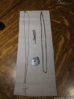 Sterling chains, pendants, and tie clip laid out on a grey cloth on a wooden surface