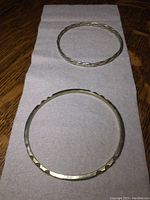 Two heavy sterling silver bracelets laid flat on a soft surface on wood background. One is twisted rope style and one has a hammered geometric pattern.