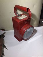 Front and side view of the red metal vintage Burgess Twin Six lantern showing large glass lens and top handle.