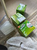 Three boxes of Swiffer Sweeper dry sweeping refills and one unopened stack of refills in plastic wrapping next to a white mop pad on carpet.