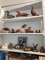 Wide view of top two shelves showing wooden and ceramic duck figurines along with books.