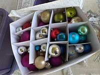 Box filled with assorted multi-colored holiday ball ornaments with shiny, matte, and glitter finishes.