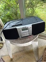 Front view of the Sony CFO-928 CD radio cassette player showing controls and display, with attached power cord, placed on table near window.