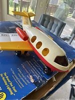 Plastic toy airplane with yellow wings, red engines, white body, and black wheels on blue box