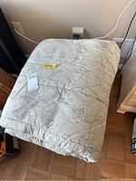 Beige/light grey king size comforter with floral embroidery folded on the floor.