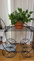 Photo of black metal plant stand holding the artificial potted plant against a curtain background, showing overall look and contents.