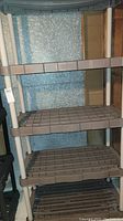 Full view of the four-tier shelving unit showing brown grid-like plastic shelves and white poles.